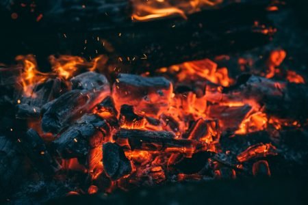 A detailed close-up of glowing embers and burning charcoal, showcasing vibrant fire textures and hues.